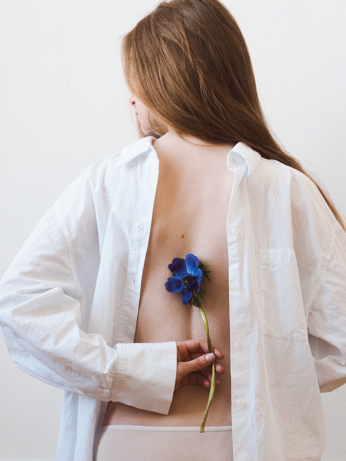 Woman holding a blue flower against her back